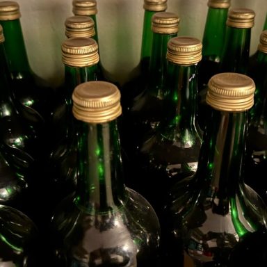 Grüne Flaschen mit goldenen Verschlüssen, eng nebeneinander angeordnet.